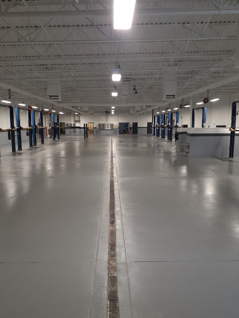 Commercial epoxy floor at turnover in a Phoenix auto service facility — coated service bays with trench drain and vehicle lifts